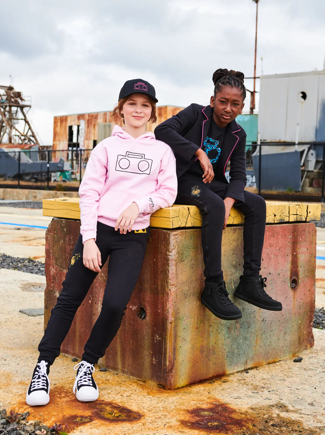 Two kids wearing StereoType Kids gender-inclusive streetwear including pink Boombox Logo Hoodie and Active Pant in urban setting