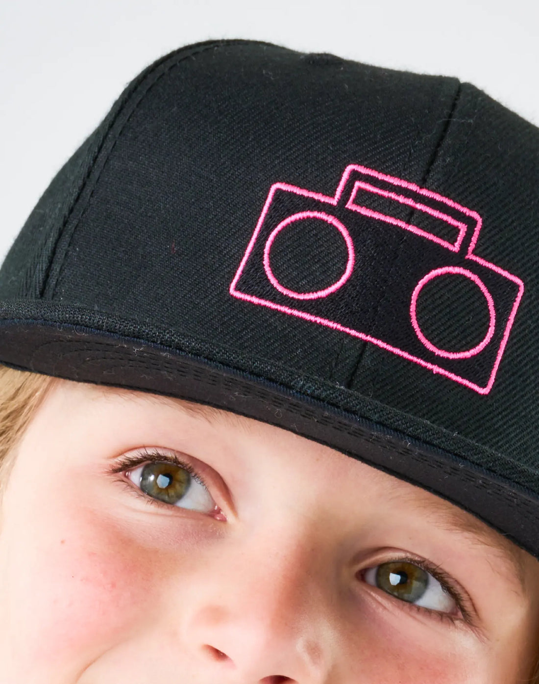 Close-up of pink boombox logo embroidery on StereoType Kids black youth Boombox Baseball Cap worn by child