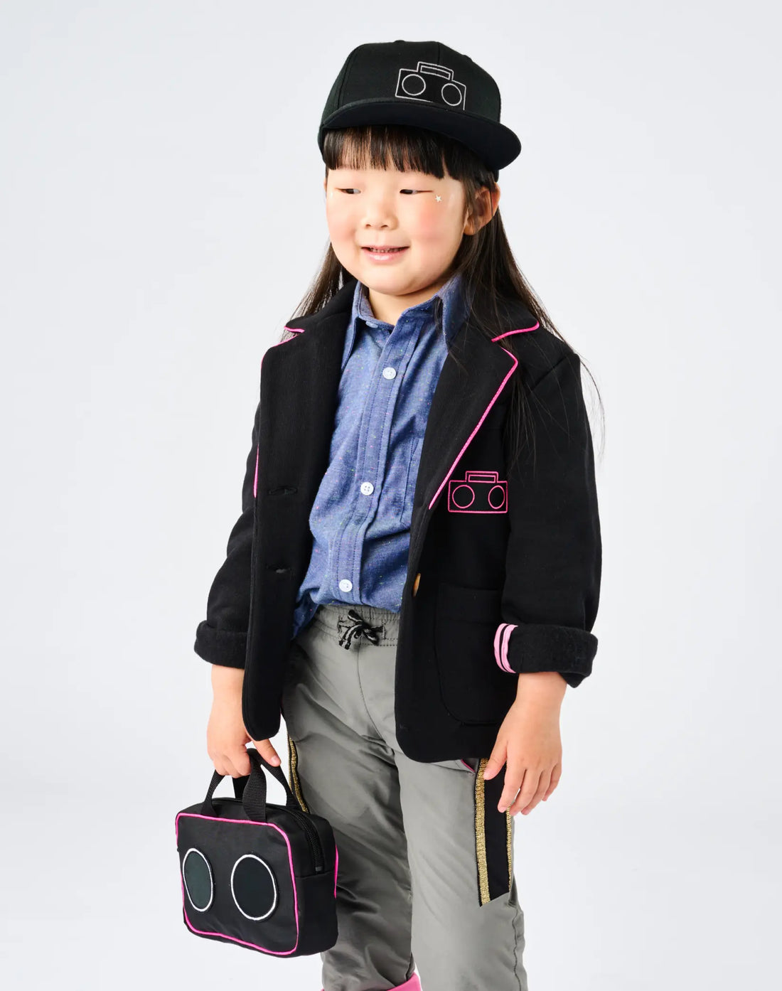 Child wearing StereoType Kids Boombox Baseball Cap with white logo, Hot Pink Boombox Blazer over Chambray Button-Down Zip Shirt, holding Boombox Treasure Bag