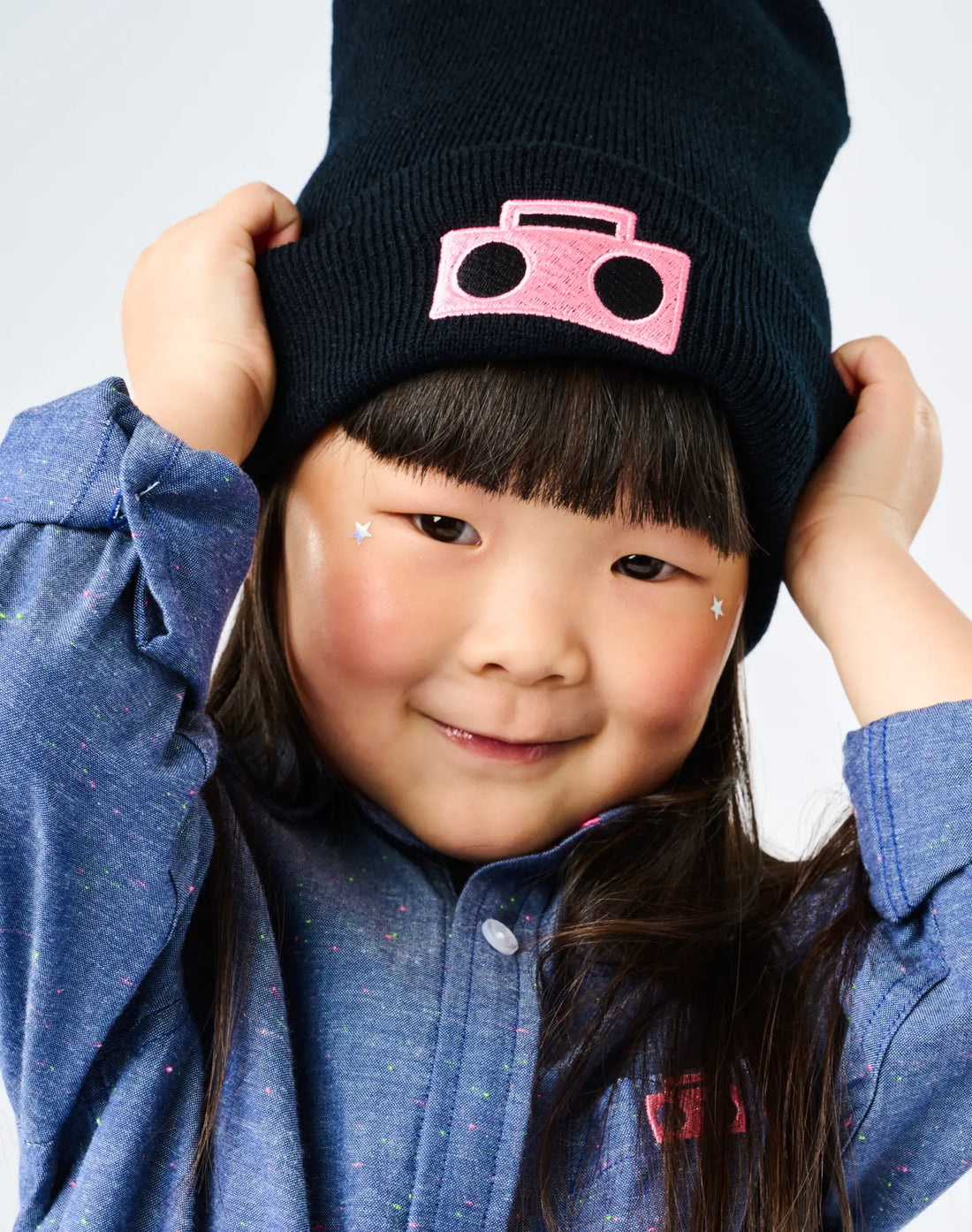 Child wearing StereoType Kids Boombox Beanie in black with hot pink embroidered Boombox patch and Chambray Button-Down Zip Shirt, unisex gender-inclusive kids and adult beanie embroidered in San Francisco