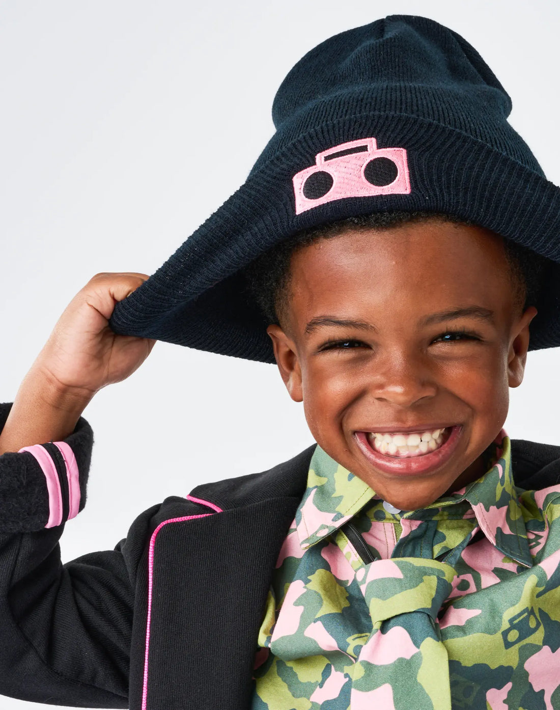 Child wearing StereoType Kids Boombox Beanie in black with hot pink embroidered Boombox patch, styled with Hot Pink Boombox Blazer and Camo Button-Down Zip Shirt, unisex gender-inclusive accessory