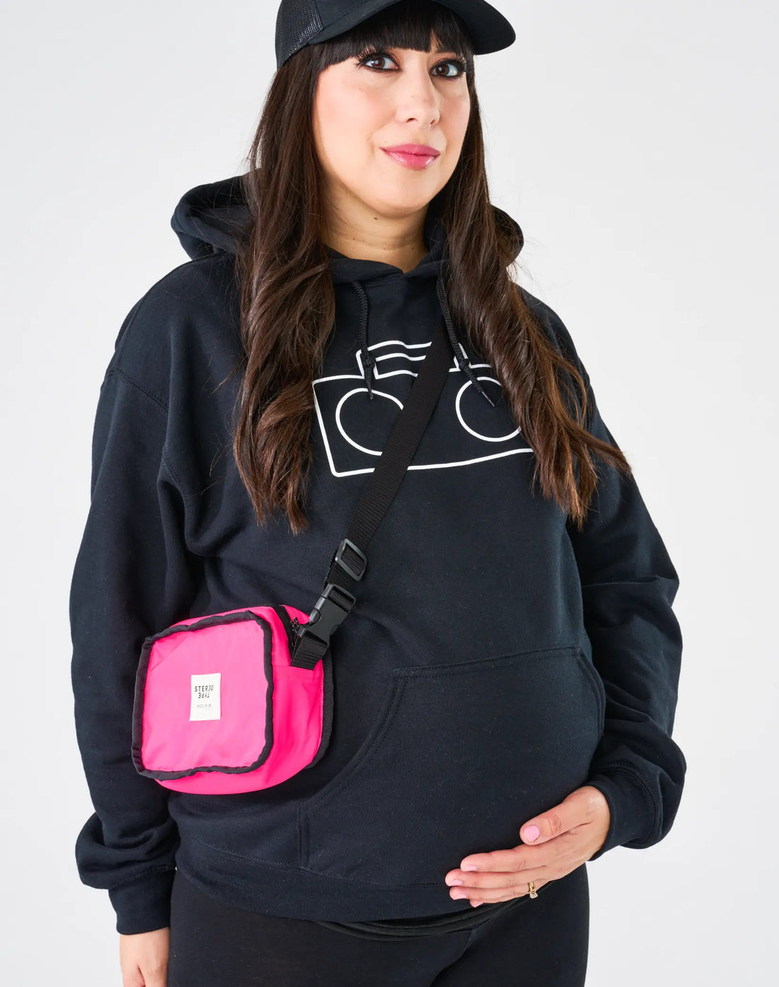 Adult wearing StereoType Kids black Boombox Logo Hoodie with pink StereoType crossbody Boombox Treasure Bag and black Boombox Trucker Cap