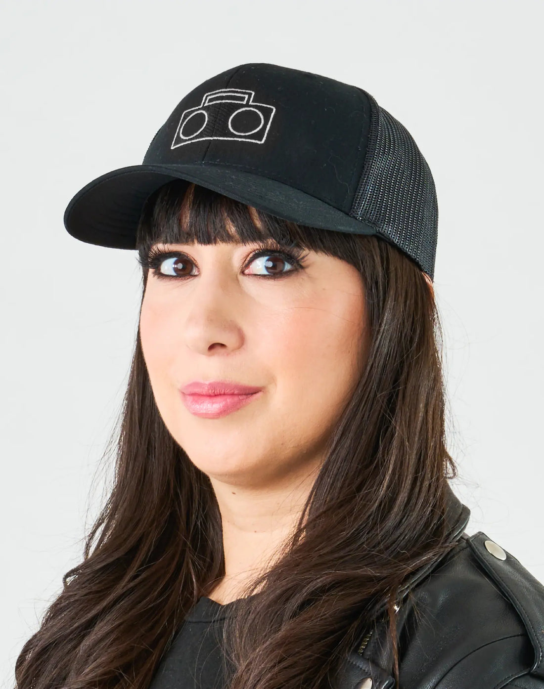 Adult wearing StereoType Kids black Boombox Trucker Cap with white embroidered logo and black leather jacket