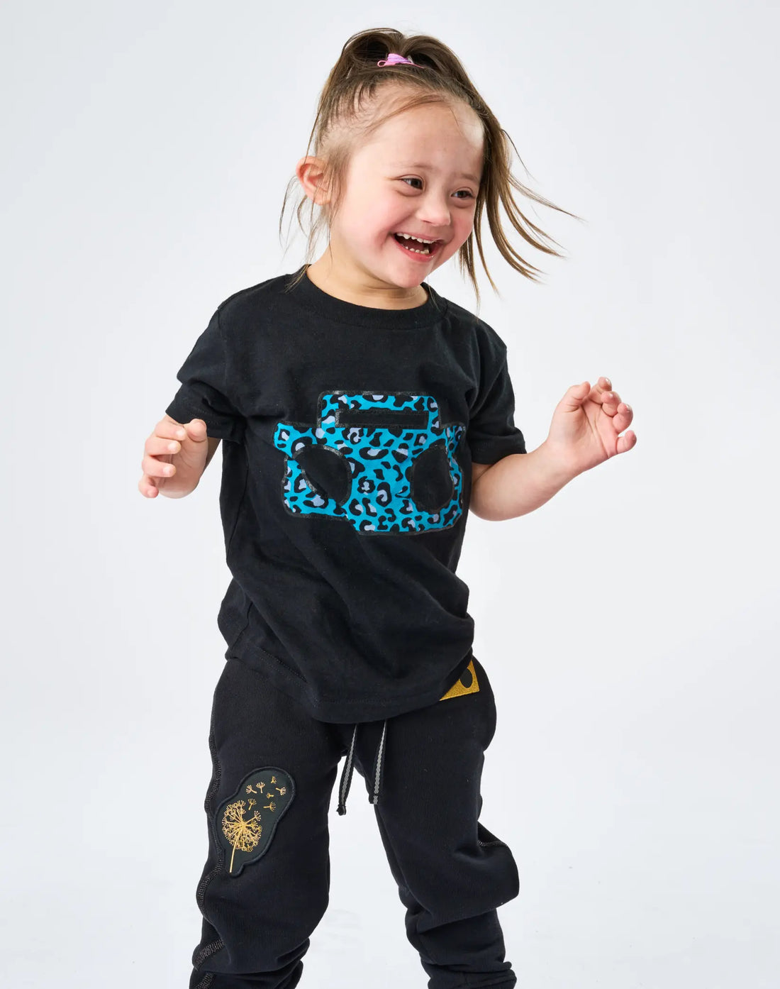 Child dancing wearing StereoType Kids Cheetah Boombox unisex kids black graphic tee with Boombox Knit Sweatpants with gold Dandelion embroidered patch, gender-inclusive fashion