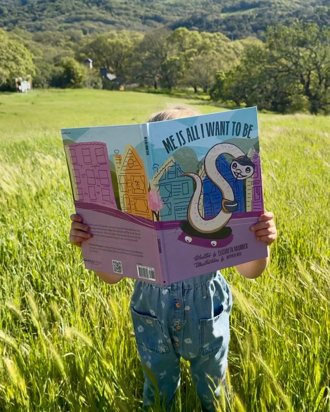 Child reading Me Is All I Want To Be hardcover book by Elizabeth Brunner in a sunny green field
