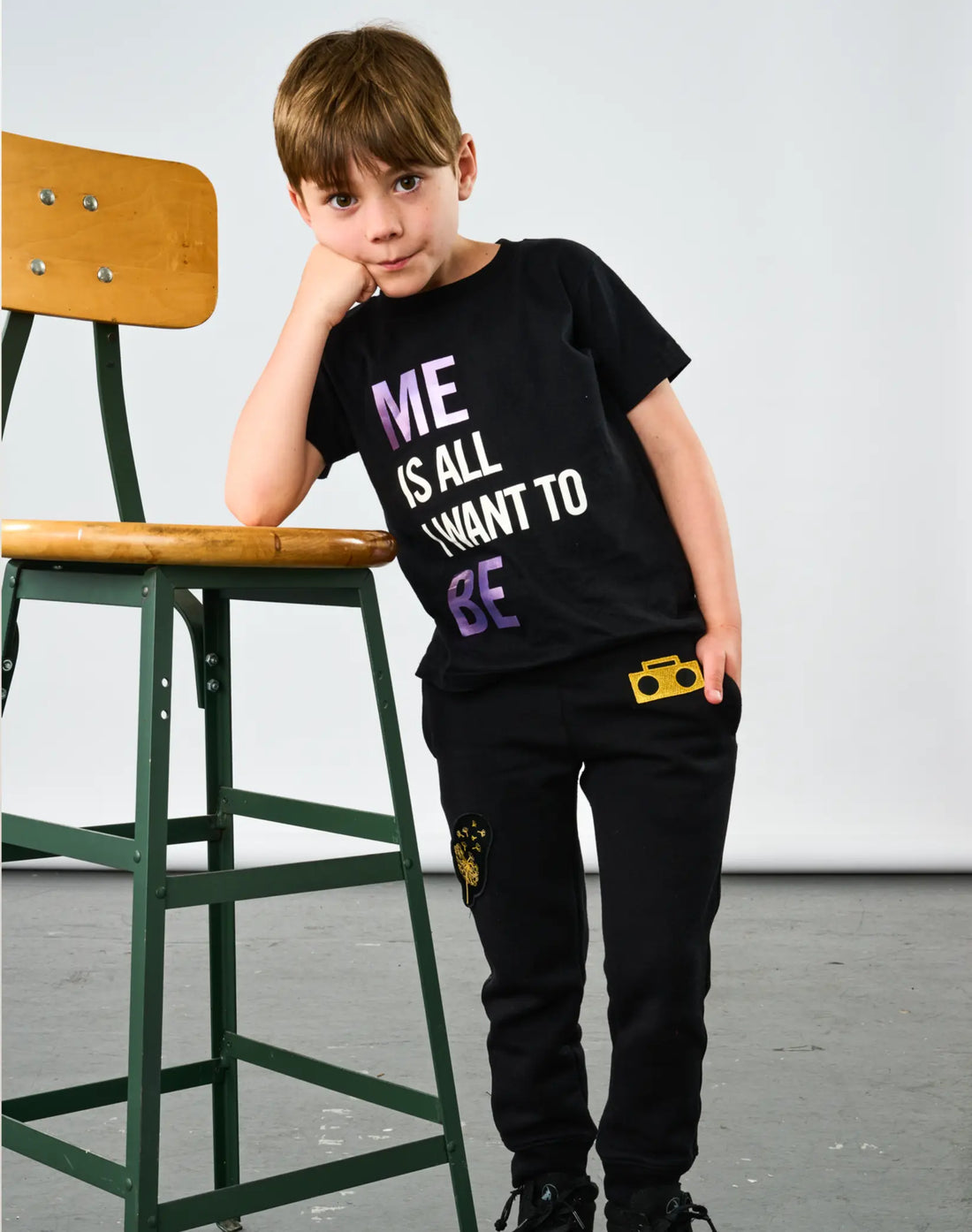 Child wearing StereoType Kids Me Is All I Want To Be unisex kids black graphic tee with holographic lettering, styled with Boombox Knit Sweatpants
