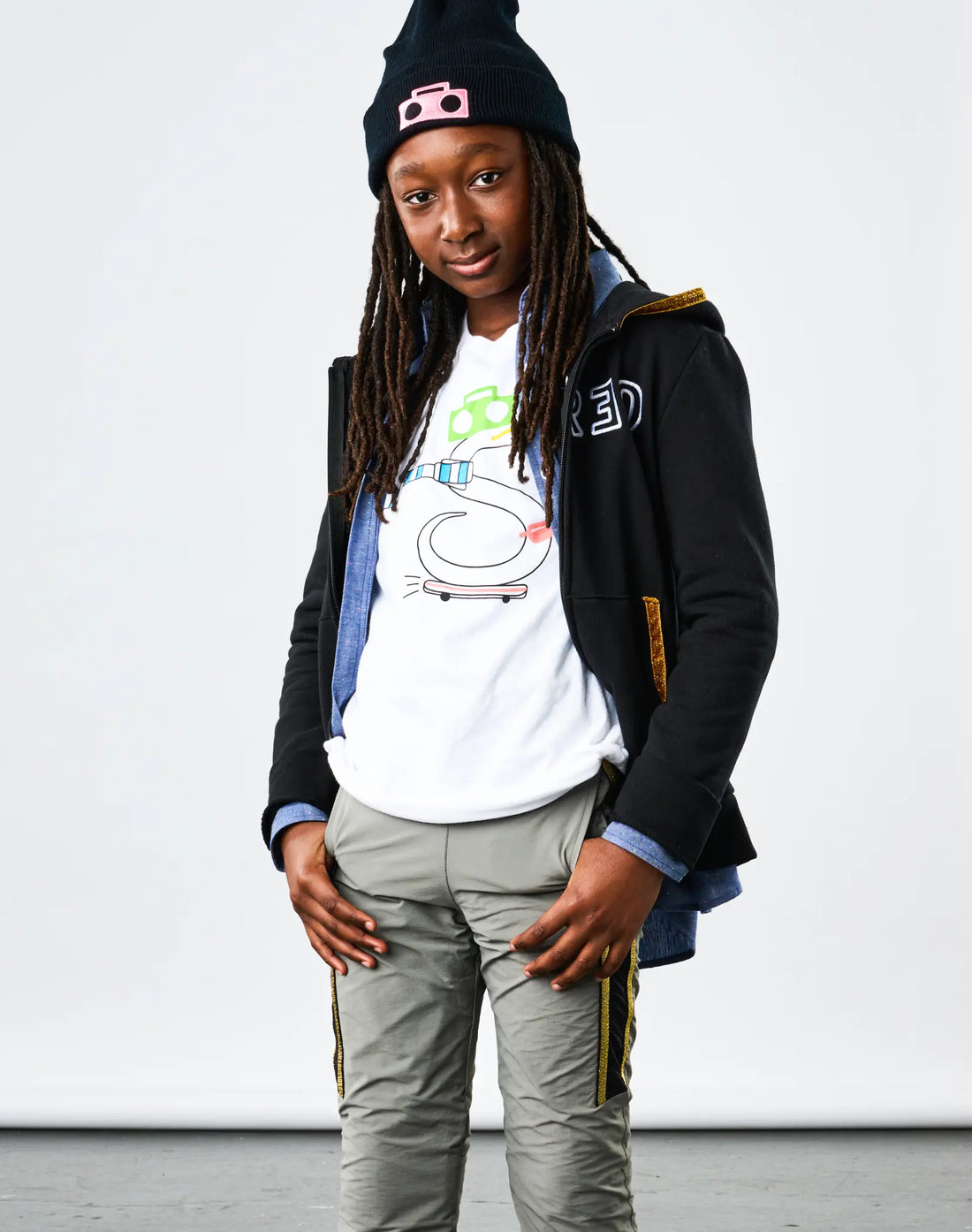 Child wearing StereoType Kids OG Stereo the Snake unisex kids white graphic tee layered under Chambray Zip Shirt and Embroidered Sparkle Zip Hoodie with Boombox Knit Beanie and Active Pant