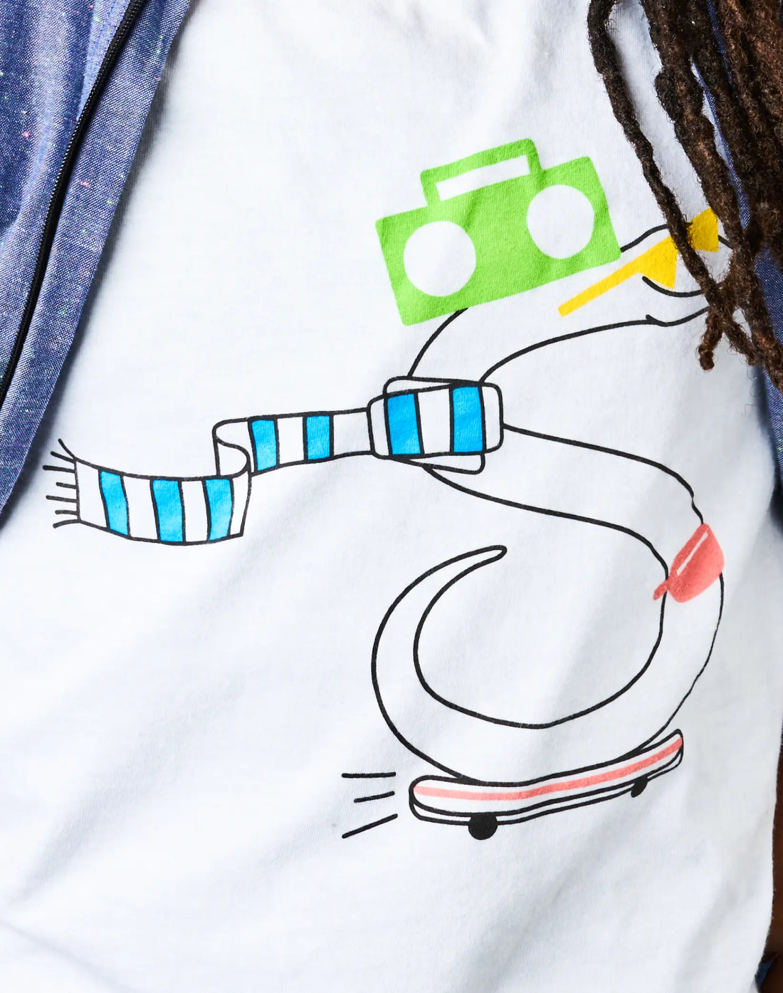 Detail of StereoType Kids OG Stereo the Snake unisex kids graphic tee showing original skateboarding snake character with green boombox hat and blue striped scarf on white cotton