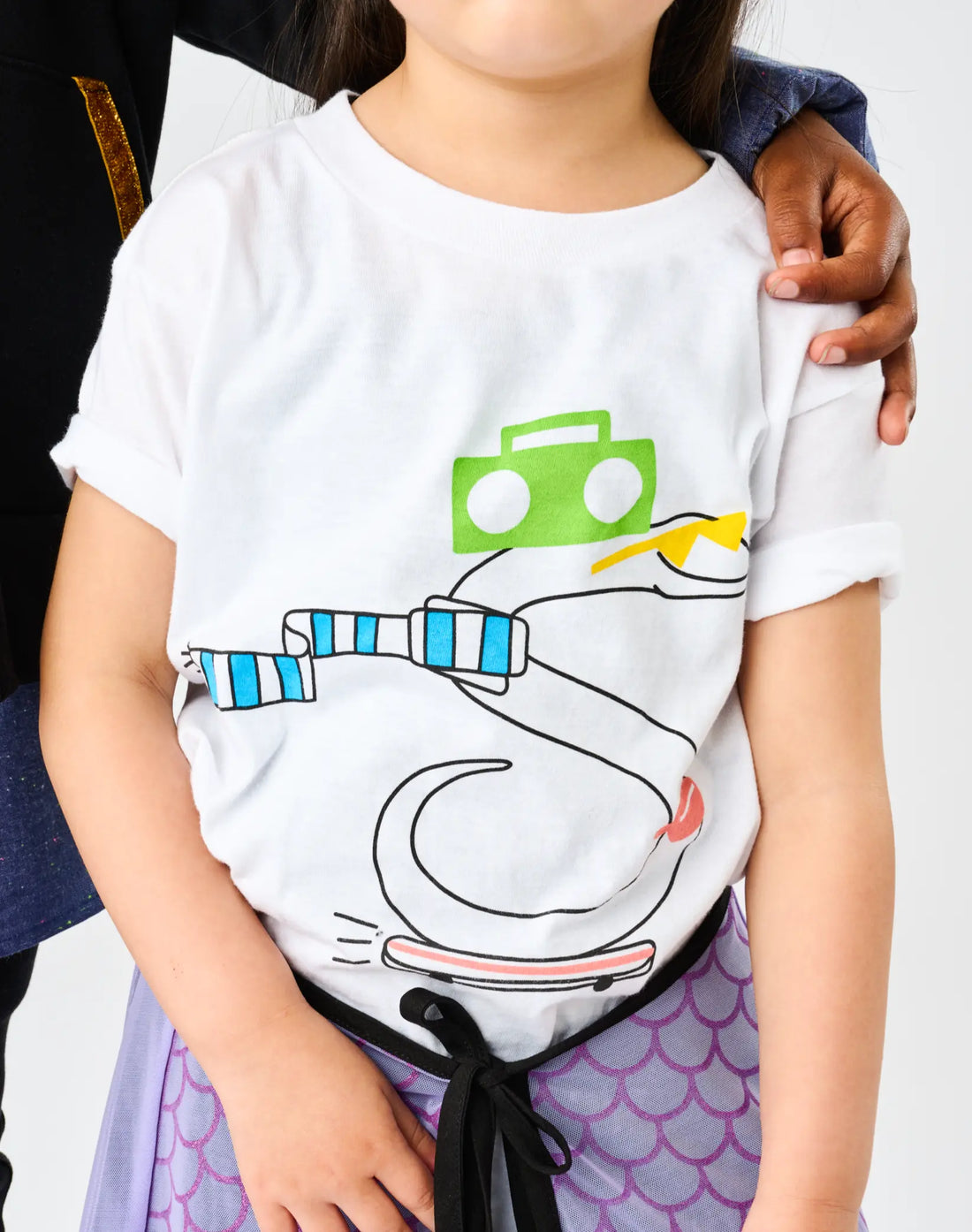 Close-up of StereoType Kids OG Stereo the Snake unisex kids white graphic tee showing skateboarding snake with green boombox and blue striped scarf, styled with Hero Skirt