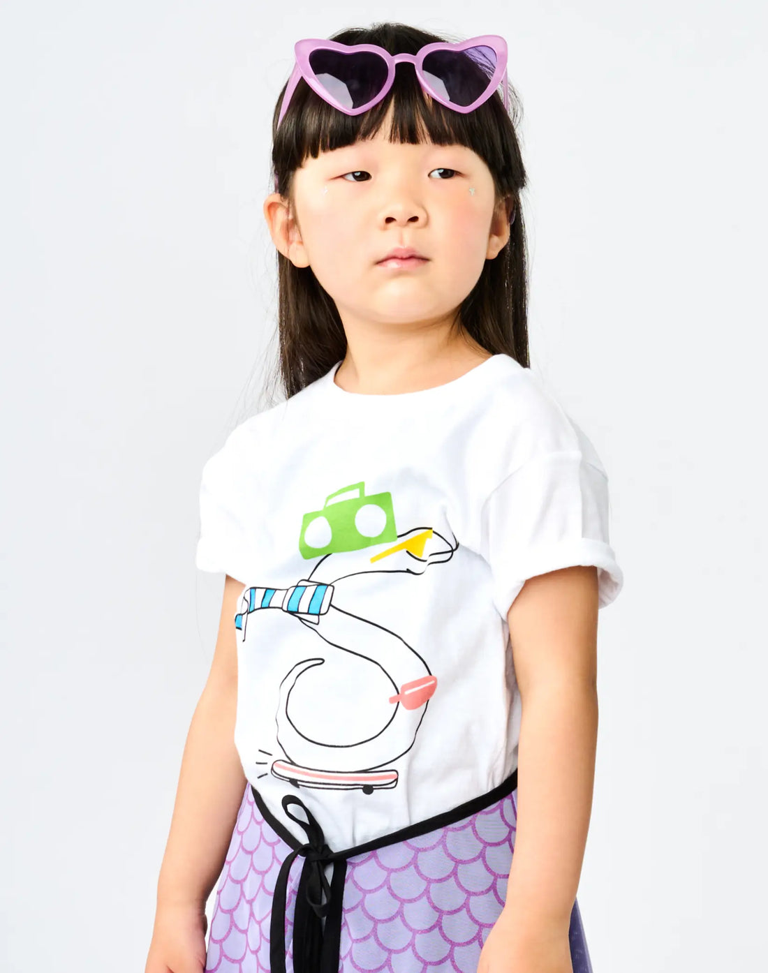 Child wearing StereoType Kids OG Stereo the Snake unisex kids white graphic tee with lavender Hero Skirt and pink heart-shaped sunglasses