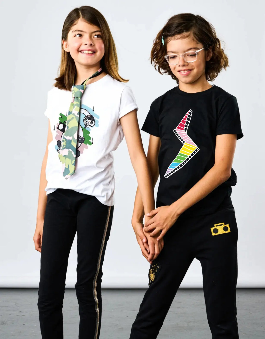 StereoType Kids co-founders Chloe and Jacob wearing Stereo the Snake white graphic tee with Camo Zip Tie and Lightning Bolt black graphic tee with Boombox Knit Sweatpants and Sparkle Leggings