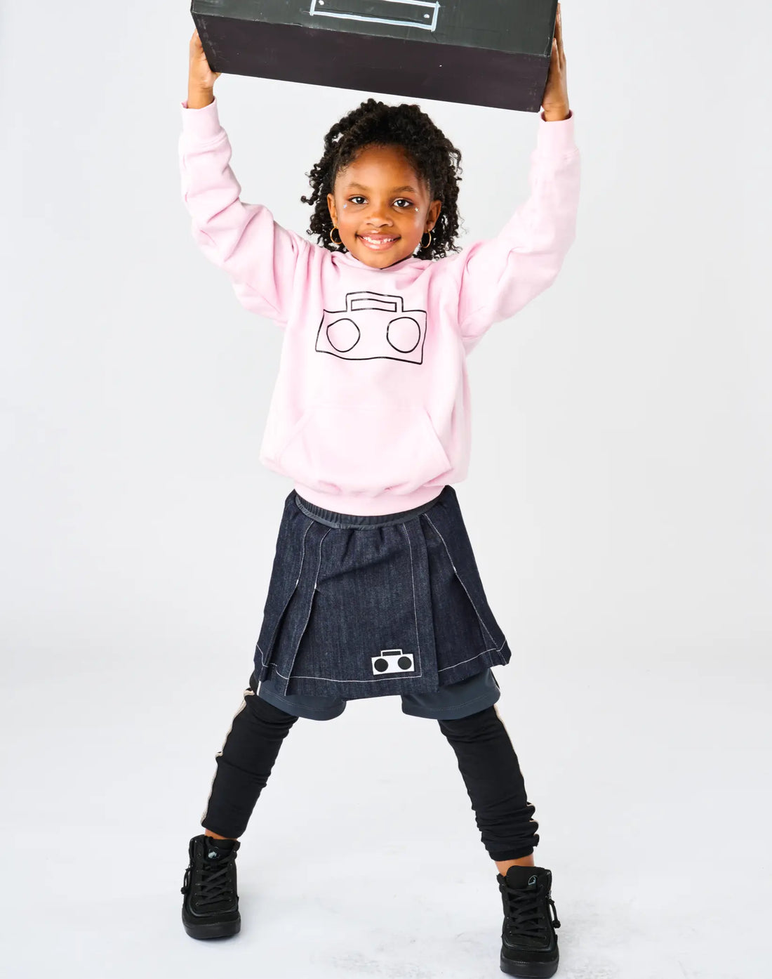 Stereotype Kids Athletic Skort worn by girl holding boombox overhead styled with pink Boombox Hoodie and black boots