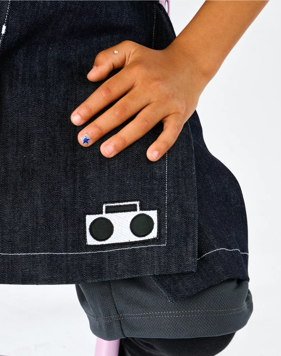 Stereotype Kids Athletic Skort closeup of white embroidered boombox logo patch on dark denim with contrast stitching