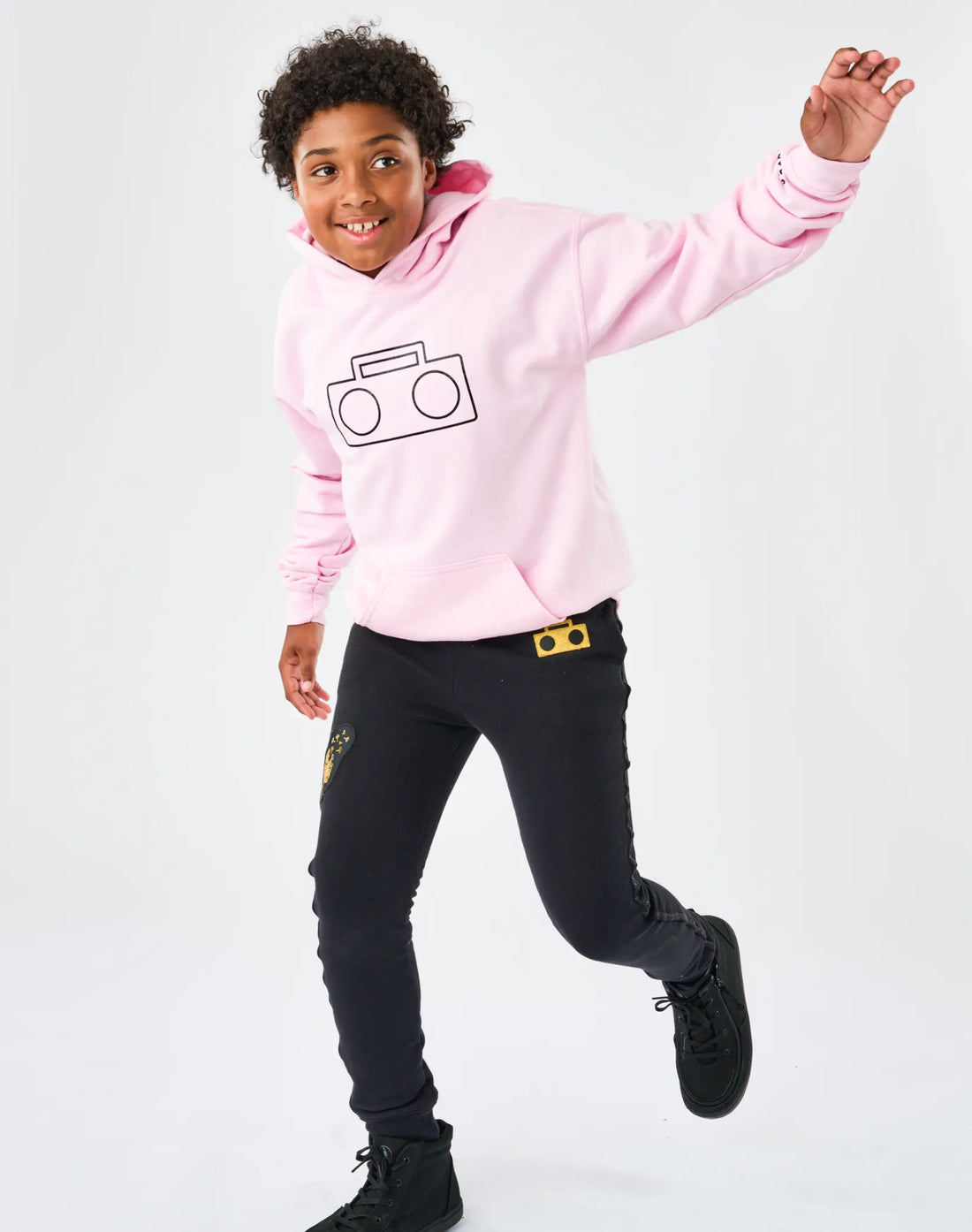 Stereotype Kids Boombox Knit Sweats in black with gold boombox patch worn by boy jumping in pink Boombox Hoodie