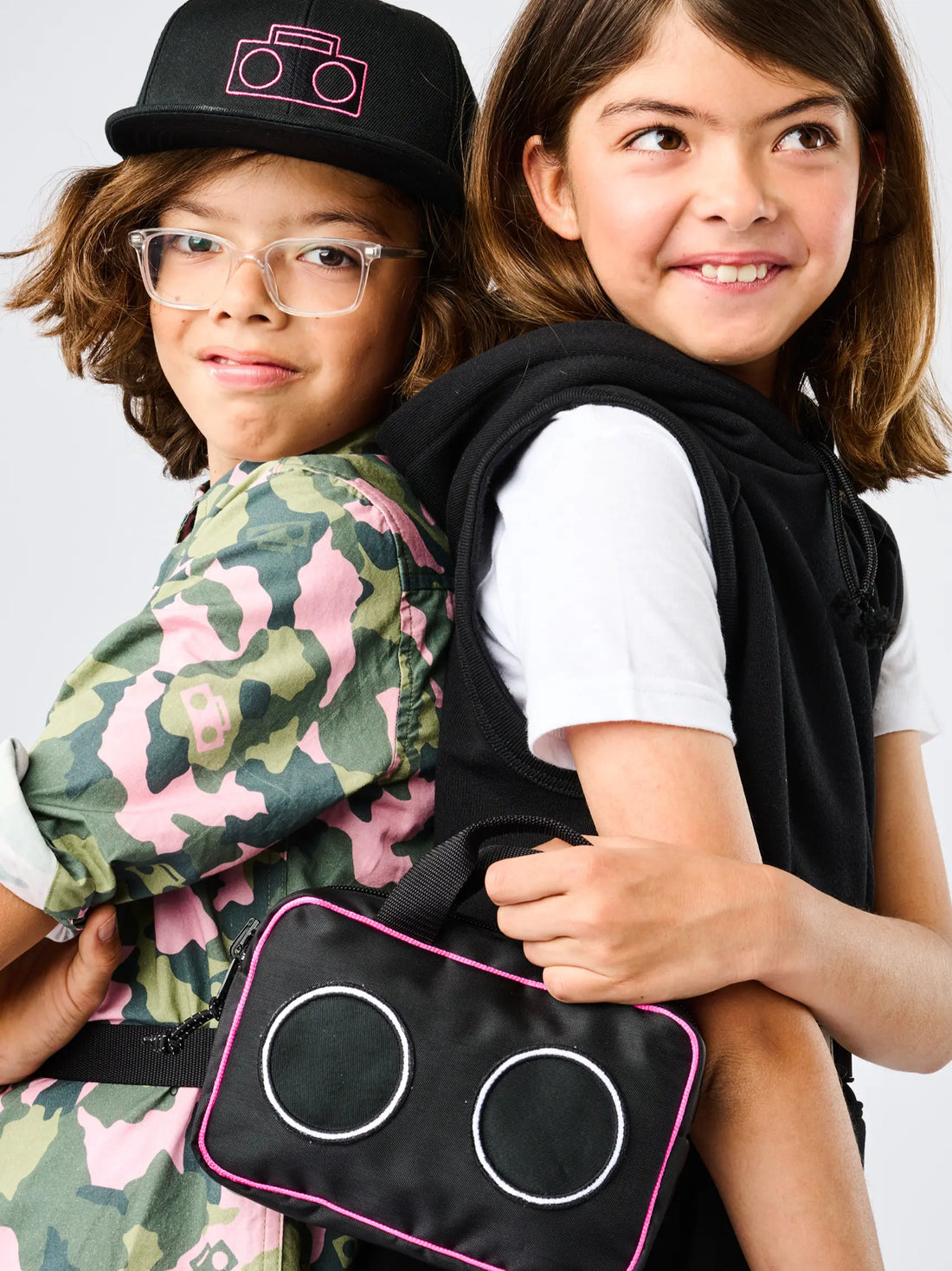StereoType Kids co-founders Chloe and Jacob wearing the Camo Button-Down Zip Shirt and holding the Boombox Treasure Bag