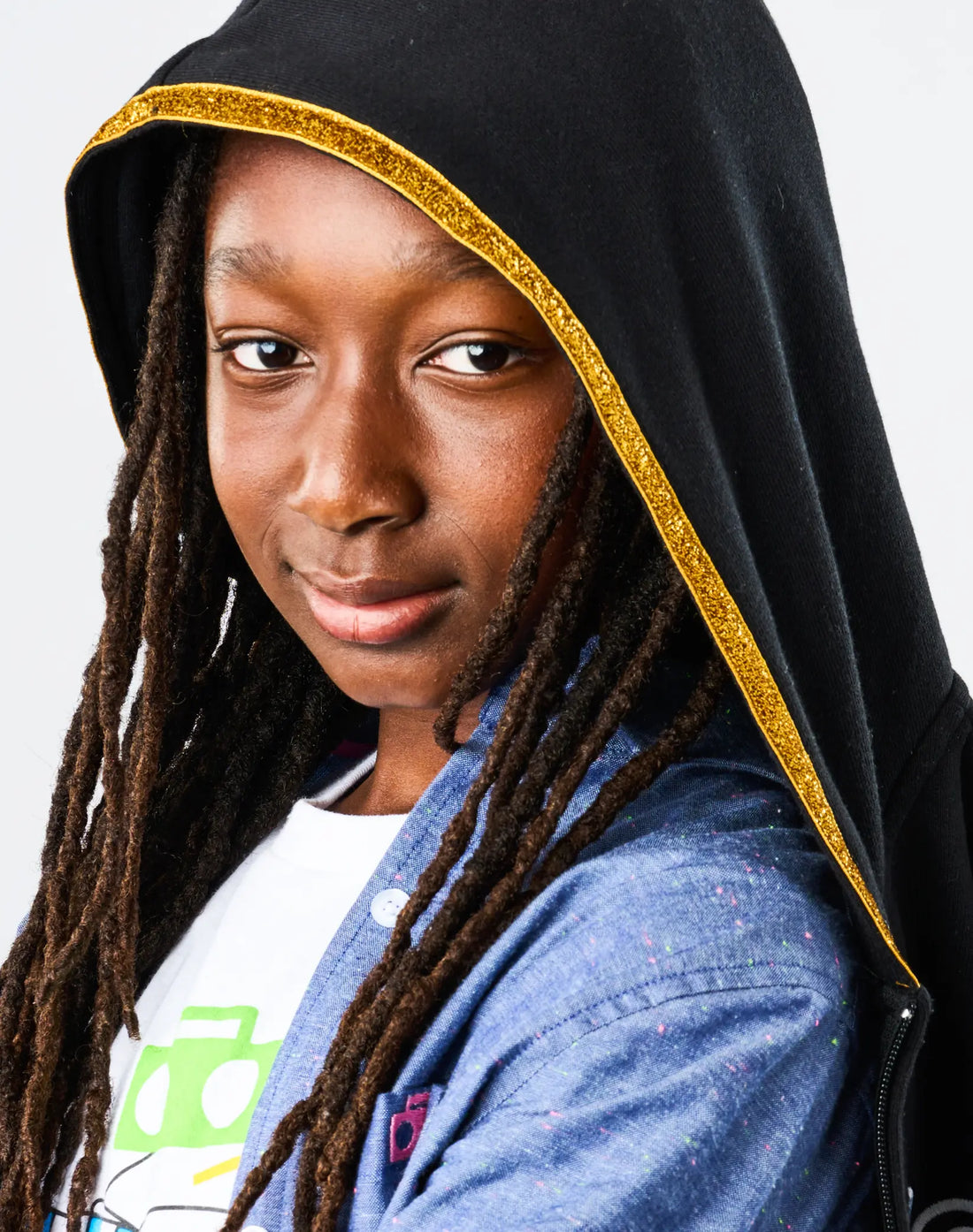 Person wearing a black hood with gold trim, blue jacket, and white shirt with green logo.