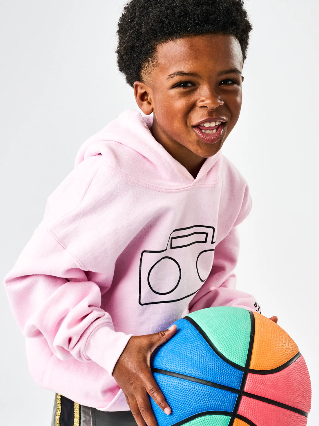 Child wearing StereoType Kids pink Boombox Logo hoodie with rainbow basketball