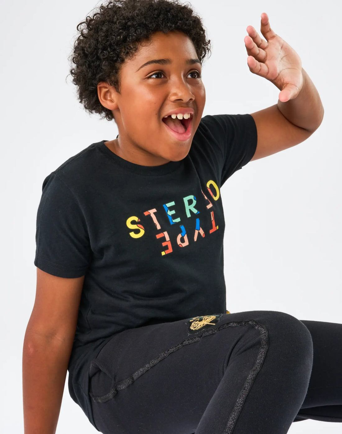 Child wearing StereoType Kids black Kaleidoscope Logo t-shirt with multicolor mirrored wordmark, gender-inclusive kids fashion