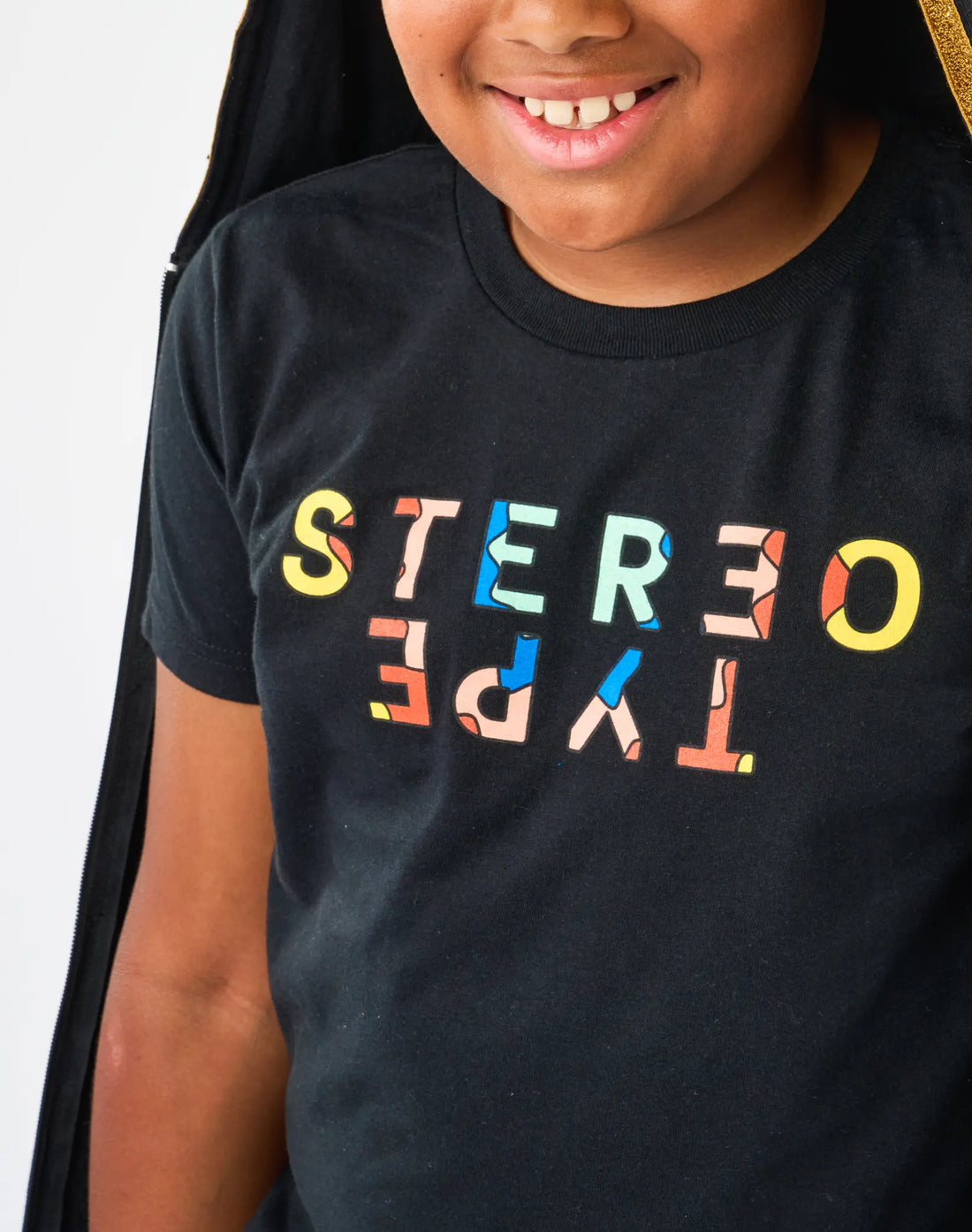 Detail of StereoType Kids Kaleidoscope Logo tee with colorful mirrored STEREOTYPE TYPE wordmark on black fabric