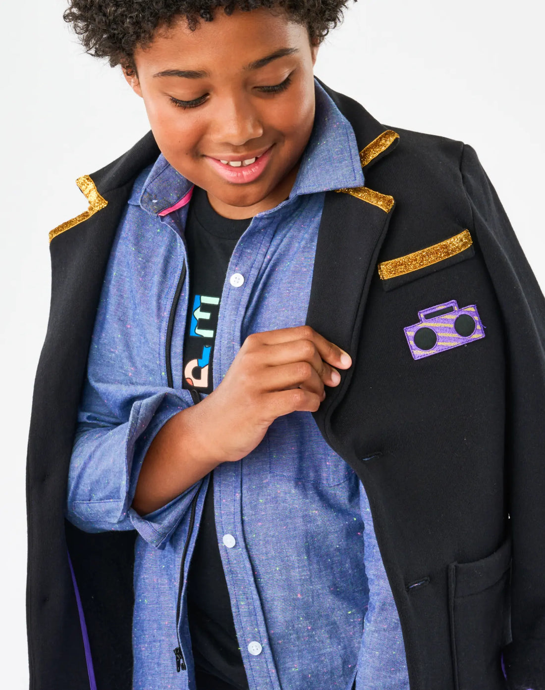 Person wearing a black jacket with gold accents and a purple boombox emblem, standing against a white background.