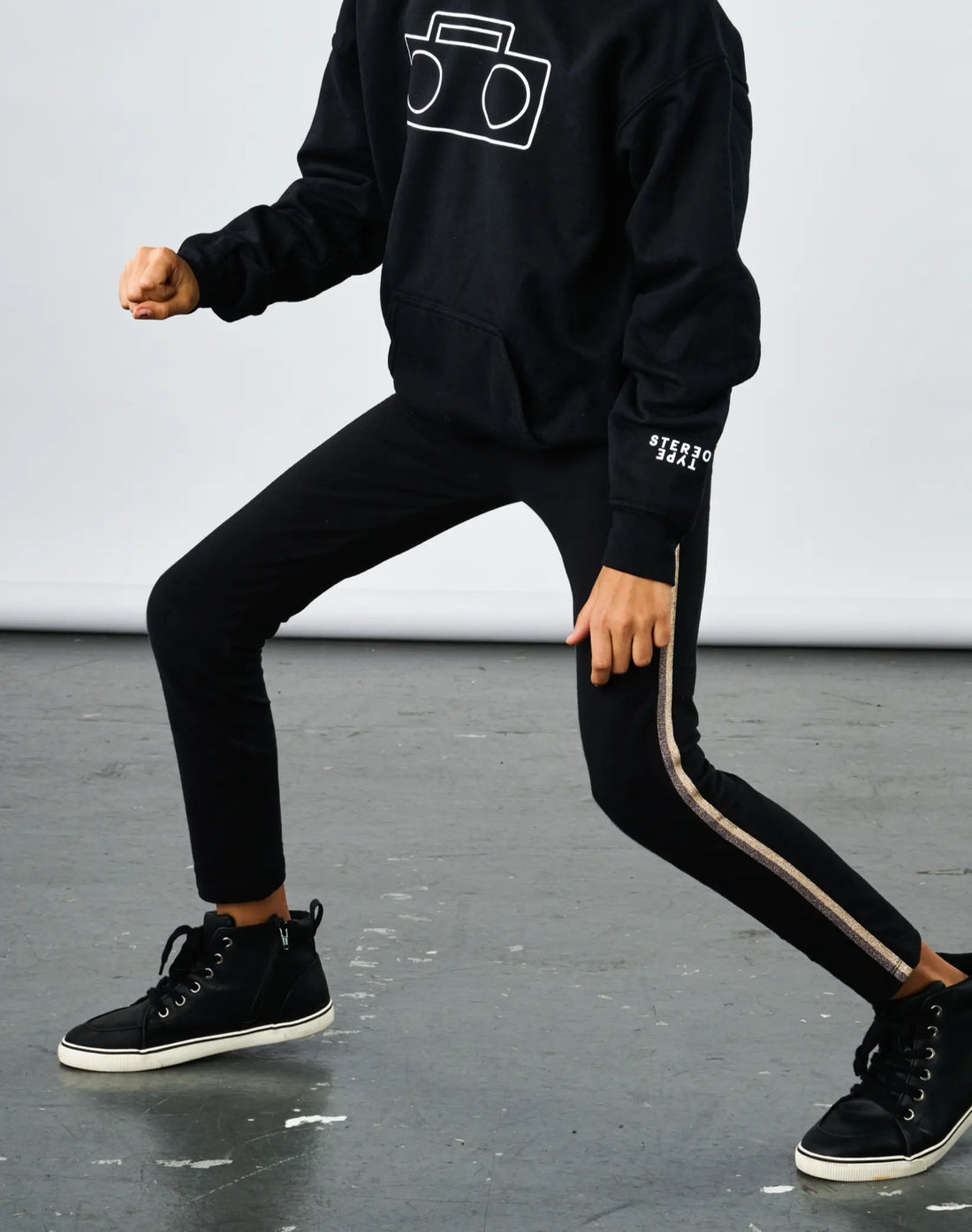 Child dancing wearing StereoType Kids Sparkle Leggings in black with gold sparkle stripe and black Boombox Logo Hoodie, unisex kids gender-inclusive fashion