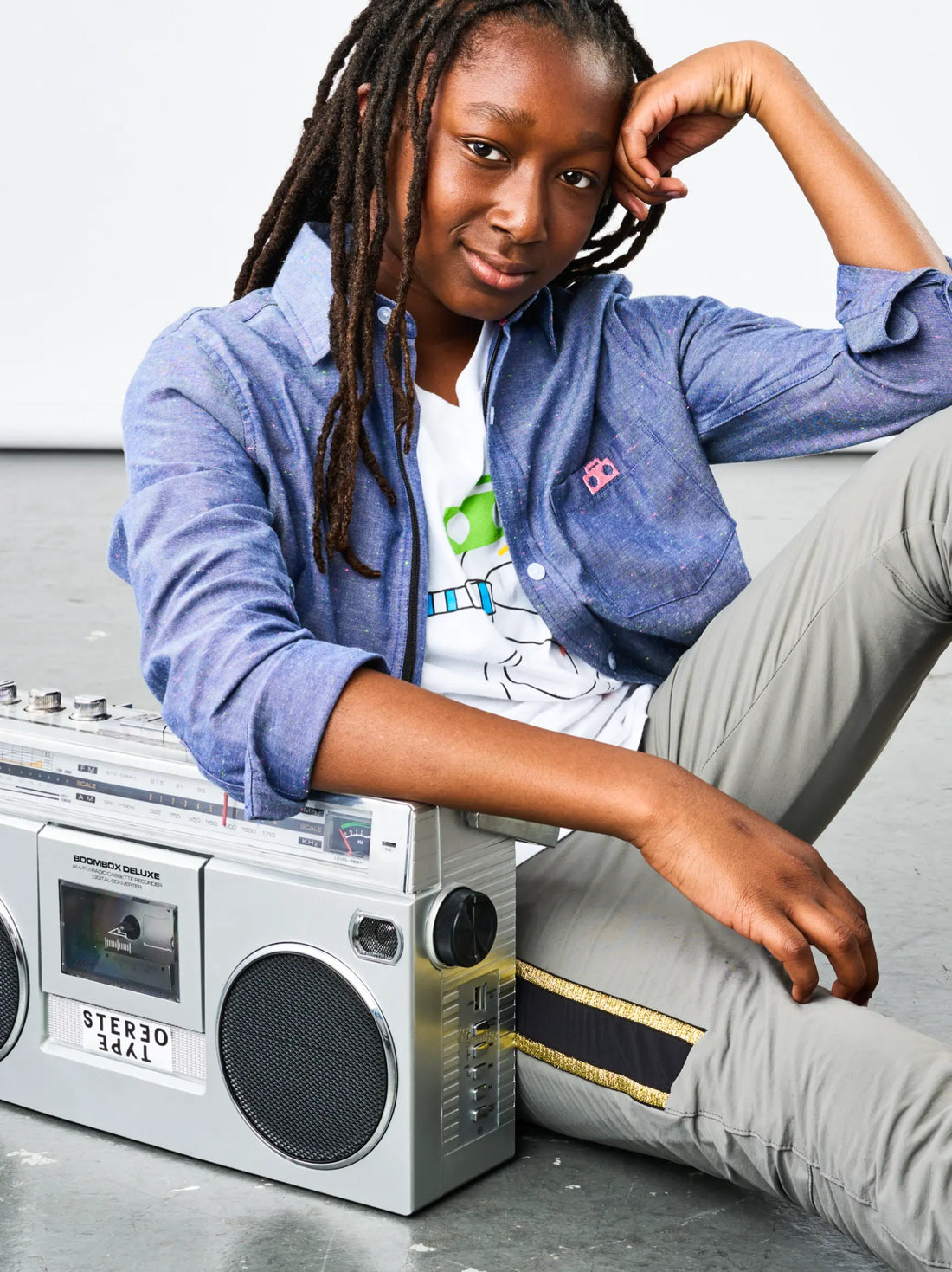hild wearing StereoType Kids Stereo the Snake tee layered under the Chambray Zip Button-Down shirt, posed with a vintage boombox